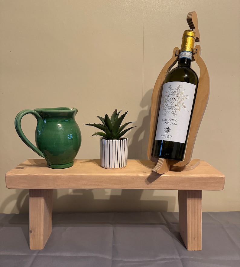 May include: A wooden wine bottle holder shaped like a bird with a green pitcher and a potted succulent plant on a wooden bench.