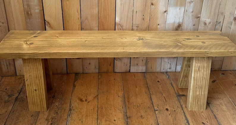 May include: A rustic wooden bench with a natural finish. The bench has a simple design with a rectangular top and two A-frame legs.