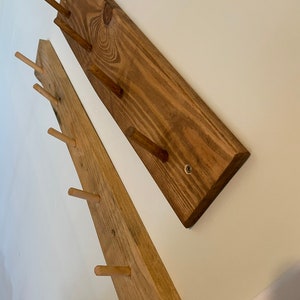 May include: Two wooden wall-mounted coat racks with multiple wooden pegs. The racks are made of natural wood with a light brown stain.
