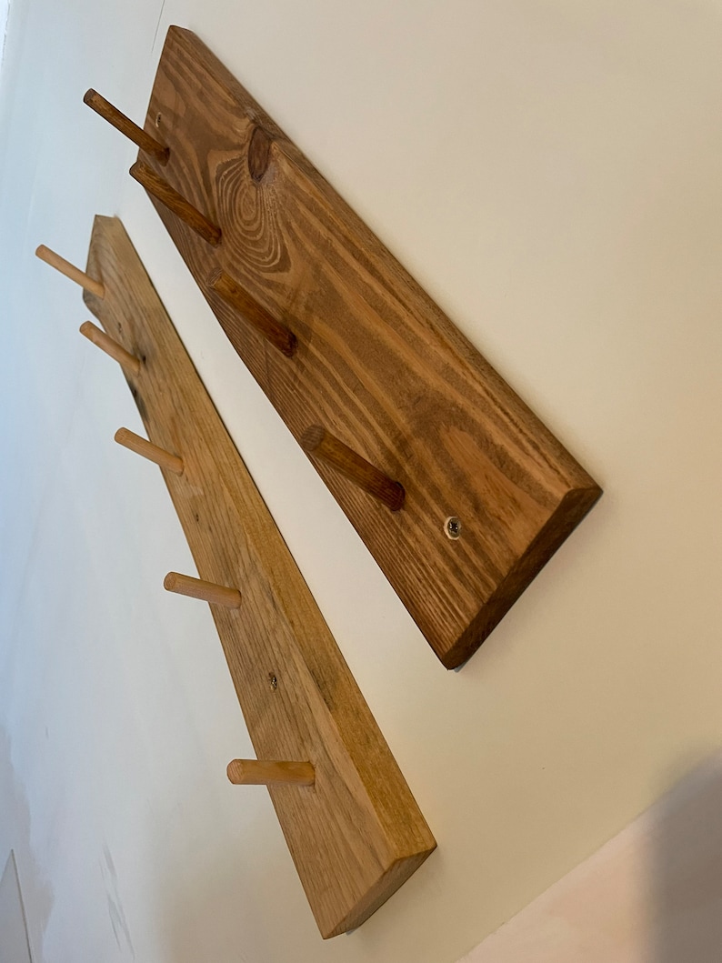 May include: Two wooden wall-mounted coat racks with multiple wooden pegs. The racks are made of natural wood with a light brown stain.