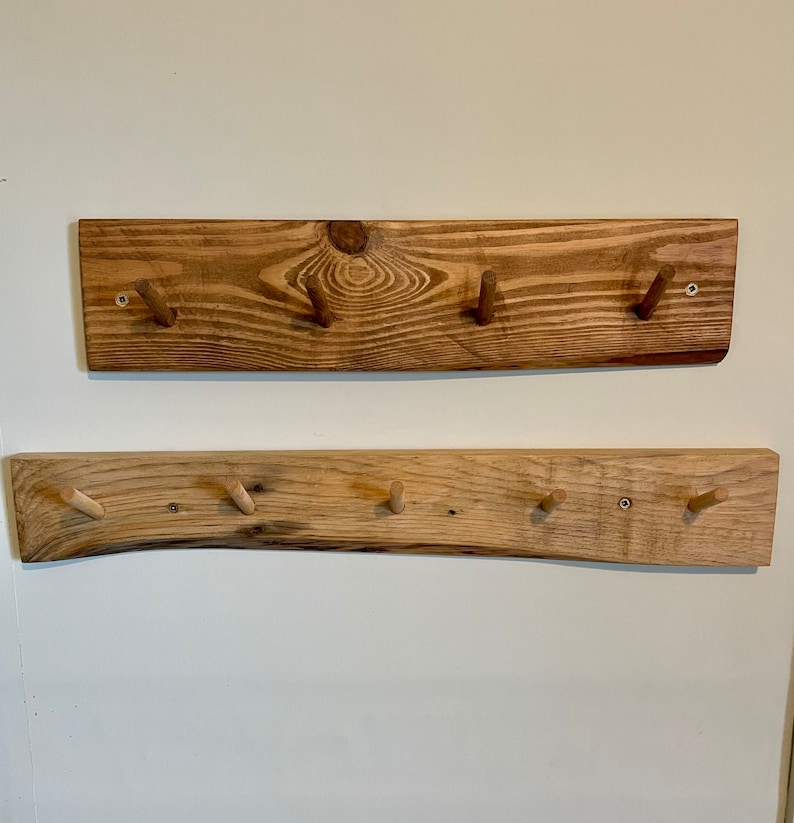 May include: Two wooden wall-mounted coat racks with natural wood tones and rounded edges. The top rack has three hooks and the bottom rack has five hooks.