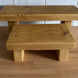 May include: Two wooden steps, one on top of the other, both made of natural wood with a light brown stain. The steps are sturdy and have a rustic look.