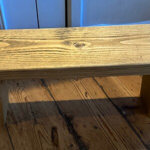 May include: A rustic wooden bench with a natural wood finish. The bench has a simple design with two legs and a rectangular top.