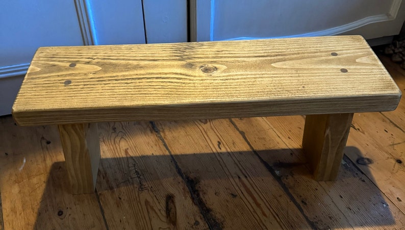 May include: A rustic wooden bench with a natural wood finish. The bench has a simple design with two legs and a rectangular top.