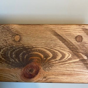 May include: Close-up of a wooden shelf with a knot and two small holes. The shelf is stained a light brown colour.