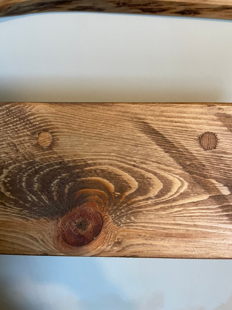 May include: Close-up of a wooden shelf with a knot and two small holes. The shelf is stained a light brown colour.