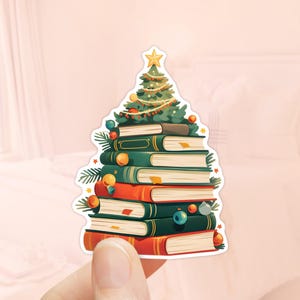 Könnte beinhalten: Ein Weihnachtsbaum aus gestapelten Büchern mit grünen, roten und goldenen Ornamenten. Der Baum ist mit einem gelben Stern oben verziert.