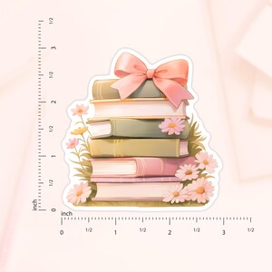 May include: A stack of five books with a pink bow on top. The books are surrounded by pink flowers and green leaves.