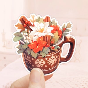 May include: A brown ceramic mug with a snowflake pattern filled with a festive arrangement of white and red flowers, cinnamon sticks, and green leaves.