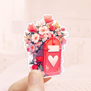 May include: A red mailbox with a heart-shaped opening and the words "Love Mail" on the front. The mailbox is overflowing with pink, white, and red flowers.