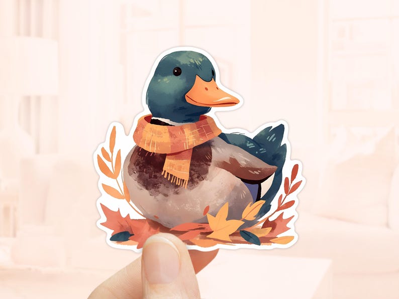 May include: A sticker featuring a watercolor illustration of a duck wearing a scarf. The duck has a teal head, orange beak, and a brown and white body. It is surrounded by autumn leaves and a yellow and orange scarf.