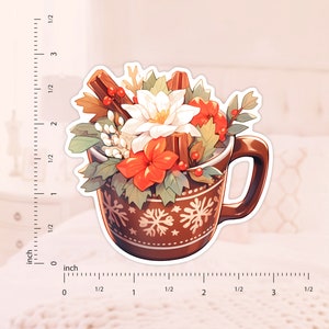 May include: A brown ceramic mug with a snowflake pattern filled with a white flower, red flowers, green leaves, and cinnamon sticks. The mug has a white outline.
