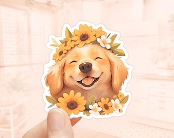 Op de afbeelding: Een golden retriever puppy met een bloemenkrans van gele zonnebloemen en witte bloemen. De puppy glimlacht met zijn ogen dicht.