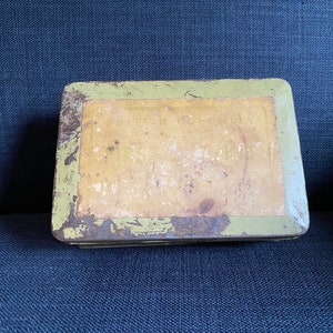 May include: A vintage green metal tin box with a yellow label. The label has faded text that is difficult to read.