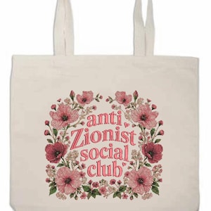 K&ouml;nnte beinhalten: Cremefarbene Tragetasche mit dem Text "anti Zionist social club" in Rosa, umgeben von einem floralen Kranz. Die Blumen sind rosa und rot, mit gr&uuml;nem Laub.
