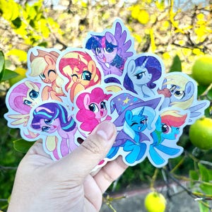 May include: A collection of die-cut vinyl stickers featuring various colorful cartoon ponies with large eyes, including characters in shades of pink, purple, blue, and yellow, with one pony wearing a blue wizard hat with yellow stars.