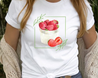 Könnte beinhalten: Weißes T-Shirt mit einer Aquarell-Illustration einer weißen Schüssel gefüllt mit roten Erdbeeren und zwei Erdbeeren an der Seite. Grüne Blätter sind um die Schüssel herum gezeichnet.