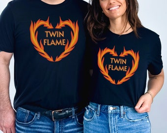 Może przedstawiać: Czarne koszulki z płomiennym wzorem w kształcie serca i napisem "TWIN FLAME" w kolorze pomarańczowym. Koszulki są noszone z niebieskimi dżinsami. Wzór przedstawia kształt serca z płomieni.