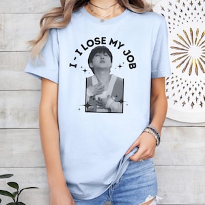 May include: Light blue t-shirt with the text "I LOSE MY JOB" in a circular design above a black and white image of a person. The image is framed by a black rectangle and star accents.