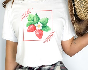 May include: White t-shirt with a red outline square featuring a watercolor illustration of two red strawberries with green leaves and a white flower.