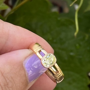 K&ouml;nnte beinhalten: Ein goldener Ring mit einem hellgelben, oval geschliffenen Edelstein. Der Ring hat ein schlichtes, elegantes Design mit einem Band von etwa 0,25 cm Breite. Der Edelstein ist in einer Zargenfassung gefasst.