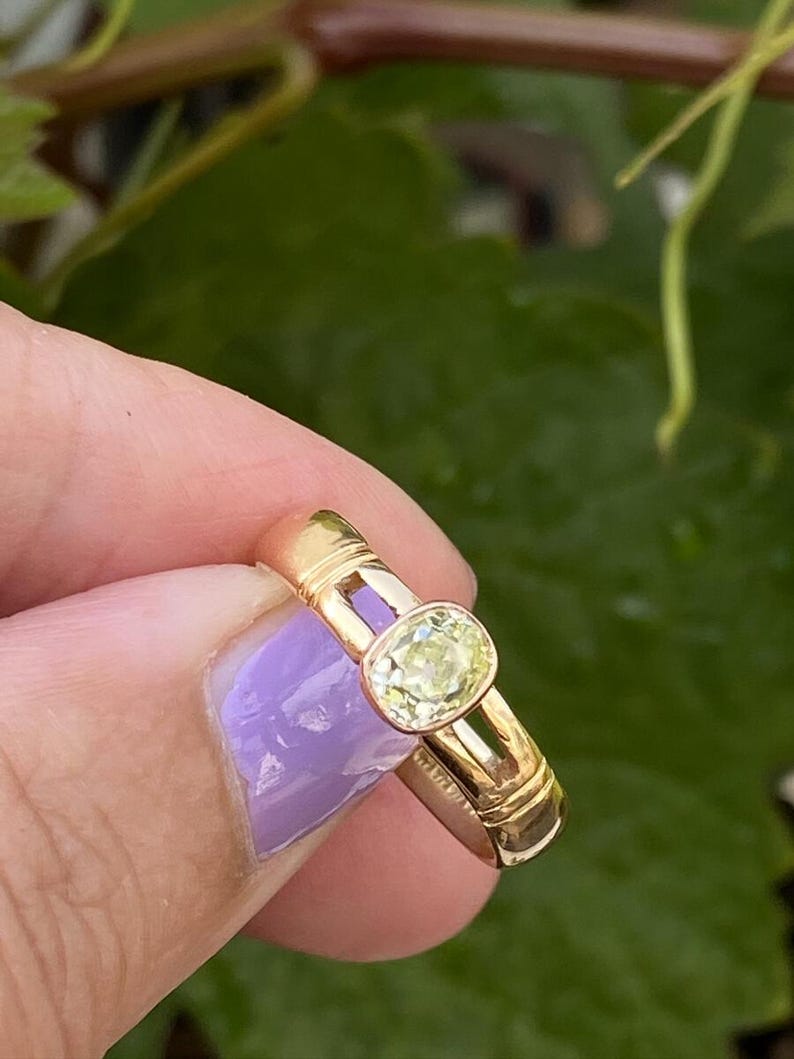 K&ouml;nnte beinhalten: Ein goldener Ring mit einem hellgelben, oval geschliffenen Edelstein. Der Ring hat ein schlichtes, elegantes Design mit einem Band von etwa 0,25 cm Breite. Der Edelstein ist in einer Zargenfassung gefasst.