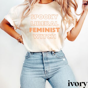 May include: A white t-shirt with the text "Spooky Liberal Feminist Witch" printed in orange.
