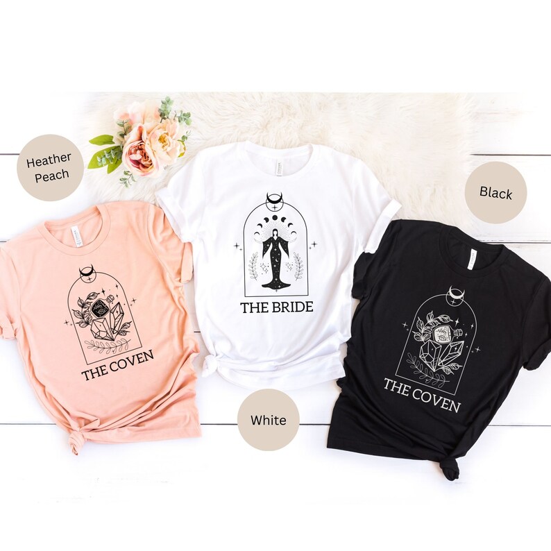 May include: Three t-shirts with different designs. The first t-shirt is peach colored with the text "The Coven" and a floral design. The second t-shirt is white with the text "The Bride" and a woman in a dress with a crescent moon and stars. The third t-shirt is black with the text "The Coven" and a floral design.