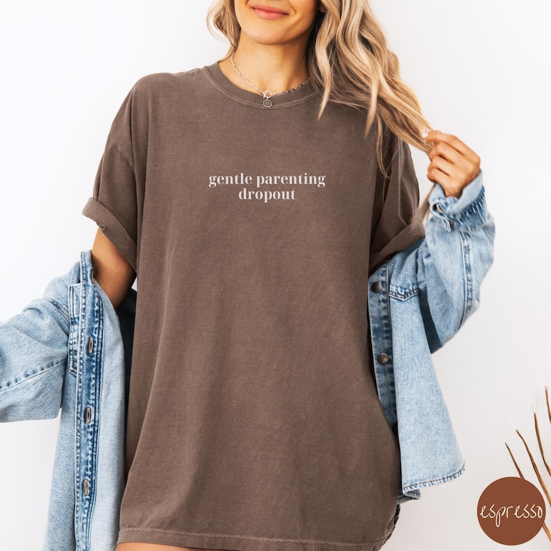 Op de afbeelding: Een oversized bruin t-shirt met de tekst "gentle parenting dropout" in wit gedrukt op de voorkant.
