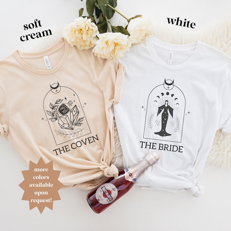 May include: Two t-shirts, one in soft cream and one in white, with a witchy design. The cream shirt says "The Coven" and features a crystal and floral design. The white shirt says "The Bride" and features a woman with a crescent moon and stars above her head.