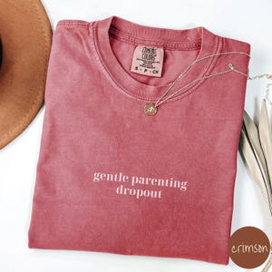 Op de afbeelding: Een t-shirt in een diepe rode kleur met de tekst "gentle parenting dropout" in wit gedrukt op de voorkant. Het shirt is gemaakt van een zacht, comfortabel materiaal en heeft een ontspannen pasvorm.
