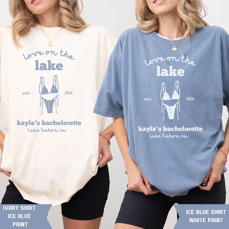 May include: Two t-shirts, one ivory and one ice blue, featuring a light blue bikini graphic and text that reads "Love on the Lake, Kayla's Bachelorette, Lake Tahoe, CA, est. 2026". The bottom of the image shows the shirt color and print color.