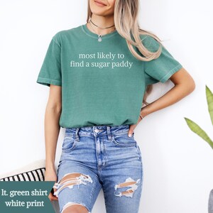 May include: A light green t-shirt with the white text "most likely to find a sugar paddy". The shirt is worn with blue jeans. The image is set against a white background.