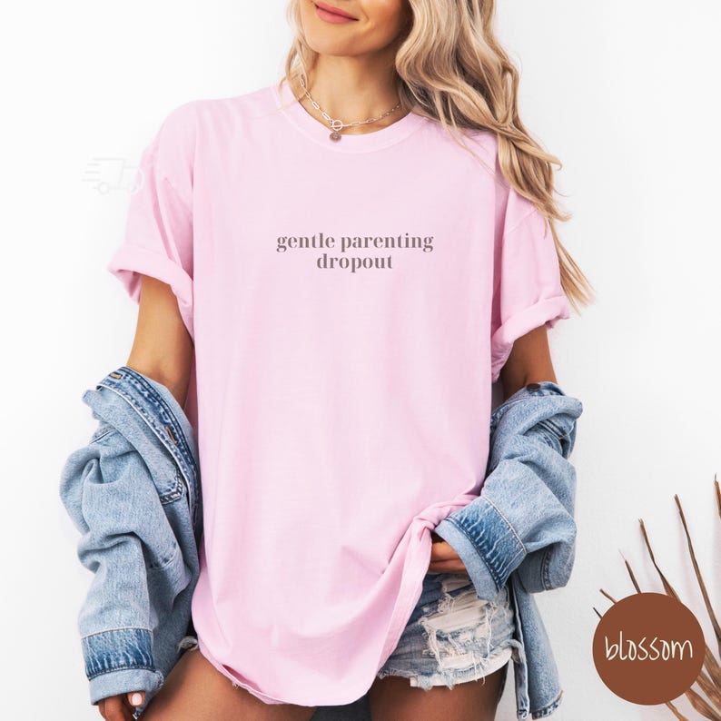 Op de afbeelding: Een roze T-shirt met de tekst "gentle parenting dropout" in lichtbruine kleur.