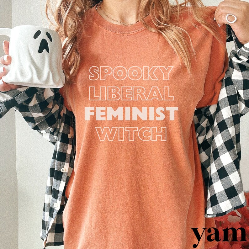 May include: A peach-colored t-shirt with the text "Spooky Liberal Feminist Witch" in white outlined letters.