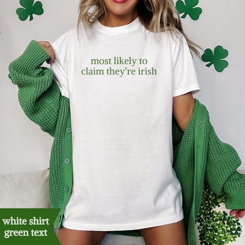 May include: White t-shirt with green text reading "most likely to claim they're irish." The shirt is worn with a green cardigan. Shamrocks are visible in the background.