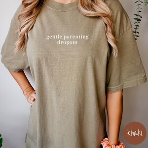 Op de afbeelding: Een kaki-kleurig T-shirt met de tekst "gentle parenting dropout" in wit gedrukt op de voorkant.
