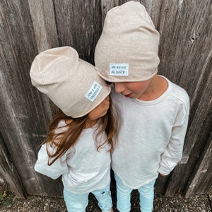 Könnte beinhalten: Zwei Kinder tragen beige Mützen mit besticktem Text. Die Mütze links sagt "Alligator &  Crocodile!" und die Mütze rechts sagt "See you later ALLIGATOR!"