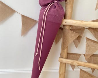 May include: A cone-shaped fabric gift bag in a deep plum color with a subtle metallic silver dot pattern. The top section features a gathered closure secured with two light pink drawstring cords that hang down the front of the pointed textile container.