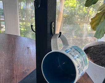 May include: Black wooden mug holder with hooks and a blue and white mug hanging from it. The holder is on a wooden table.