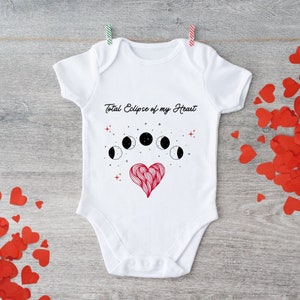 May include: White baby onesie with the text "Total Eclipse of my Heart" and a graphic of a red heart with a crescent moon design above it.