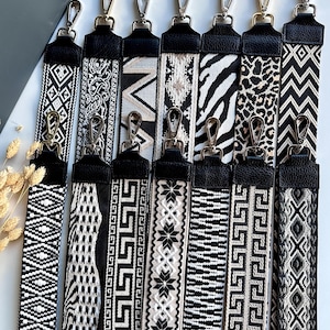 Pode incluir: Uma coleção de oito alças de bolsa estampadas em preto e branco. Cada alça apresenta um design diferente, incluindo padrões geométricos, florais e de animais. As alças têm extremidades de couro preto e fechos de metal prateado.