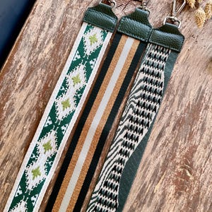 May include: Three decorative bag straps with different patterns. One strap features a white background with green geometric shapes. Another has vertical stripes in black, tan, and white. The third strap has a black and white zigzag pattern. All straps have green leather ends and silver clasps.