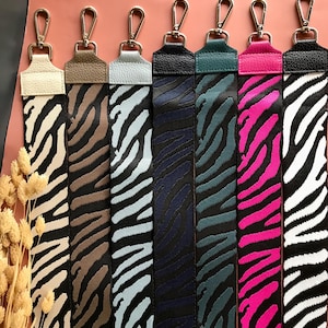 Puede incluir: Una colección de siete correas de bolso con estampado de cebra de colores con cierres metálicos plateados. Las correas presentan una variedad de colores, incluyendo beige, marrón, celeste, azul marino, verde azulado, rosa y blanco y negro. Para bolsos.