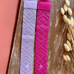 May include: Two fabric straps with gold clasps. The strap on the left is lavender with a diamond pattern and the number "8." The strap on the right is pink with a diamond pattern and the number "9."