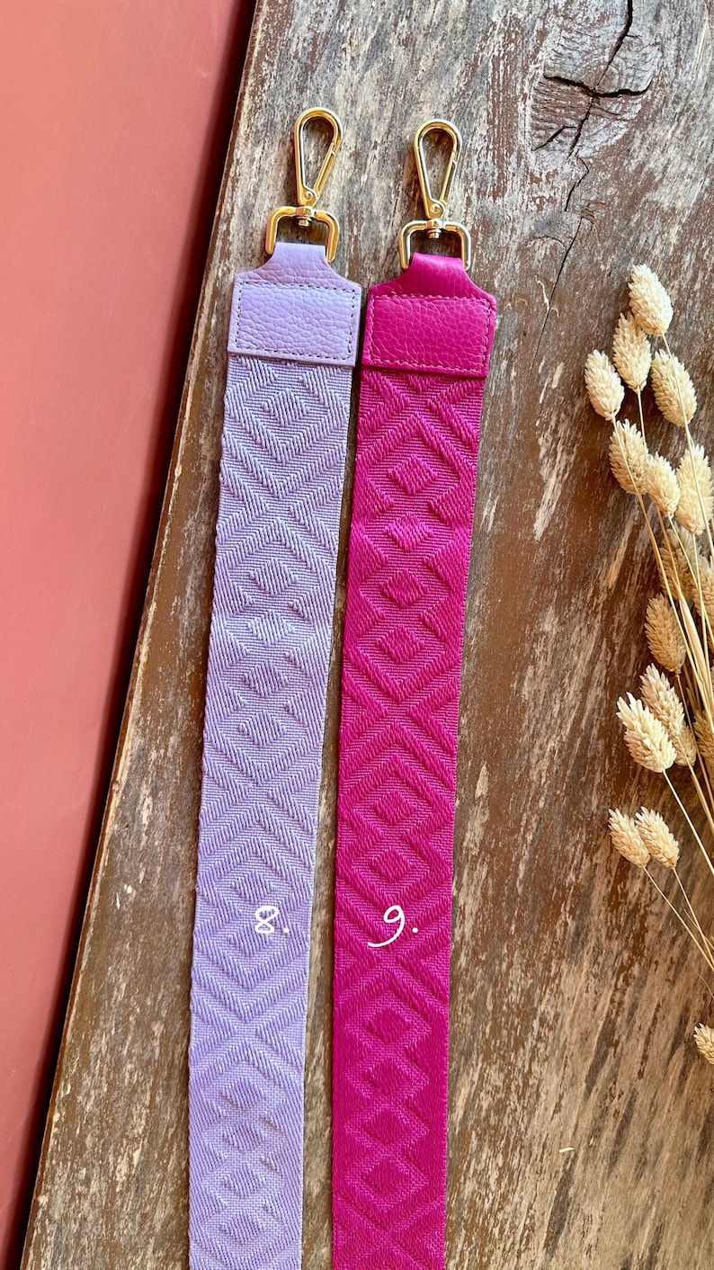 May include: Two fabric straps with gold clasps. The strap on the left is lavender with a diamond pattern and the number "8." The strap on the right is pink with a diamond pattern and the number "9."