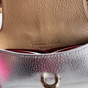 May include: Close-up of a silver leather handbag with a gold-colored clasp. The interior is a light brown color with the words "Genuine Leather Made in Italy" embossed on the leather.