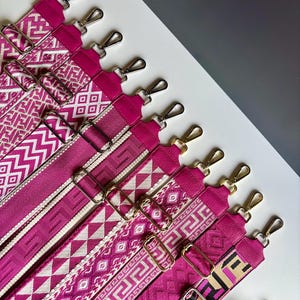 Peut inclure: Une collection de bandoulières fuchsia présentant divers motifs géométriques tissés, notamment des motifs grecs et en losange. Chaque sangle est équipée de curseurs métalliques réglables et de mousquetons pivotants argentés.