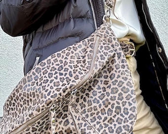 Puede incluir: Un bolso bandolera de piel con estampado de leopardo marrón y negro con cierre de cremallera. El bolso se lleva sobre una chaqueta acolchada negra.