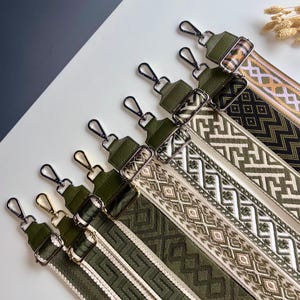 Peut inclure: Un ensemble de cinq bandoulières réglables dotées d'extrémités en similicuir vert olive et de mousquetons en métal argenté. Chaque sangle présente un motif tissé unique dans des tons vert olive, crème et noir, avec des designs géométriques variés.